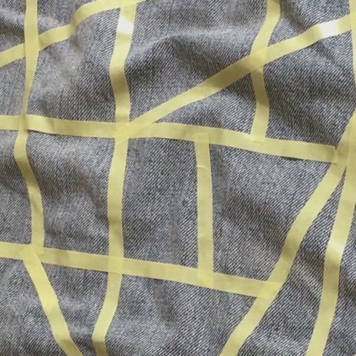 Video of tailor creating a freestyle geometric design with thin yellow tape on a light wash denim trucker jacket.