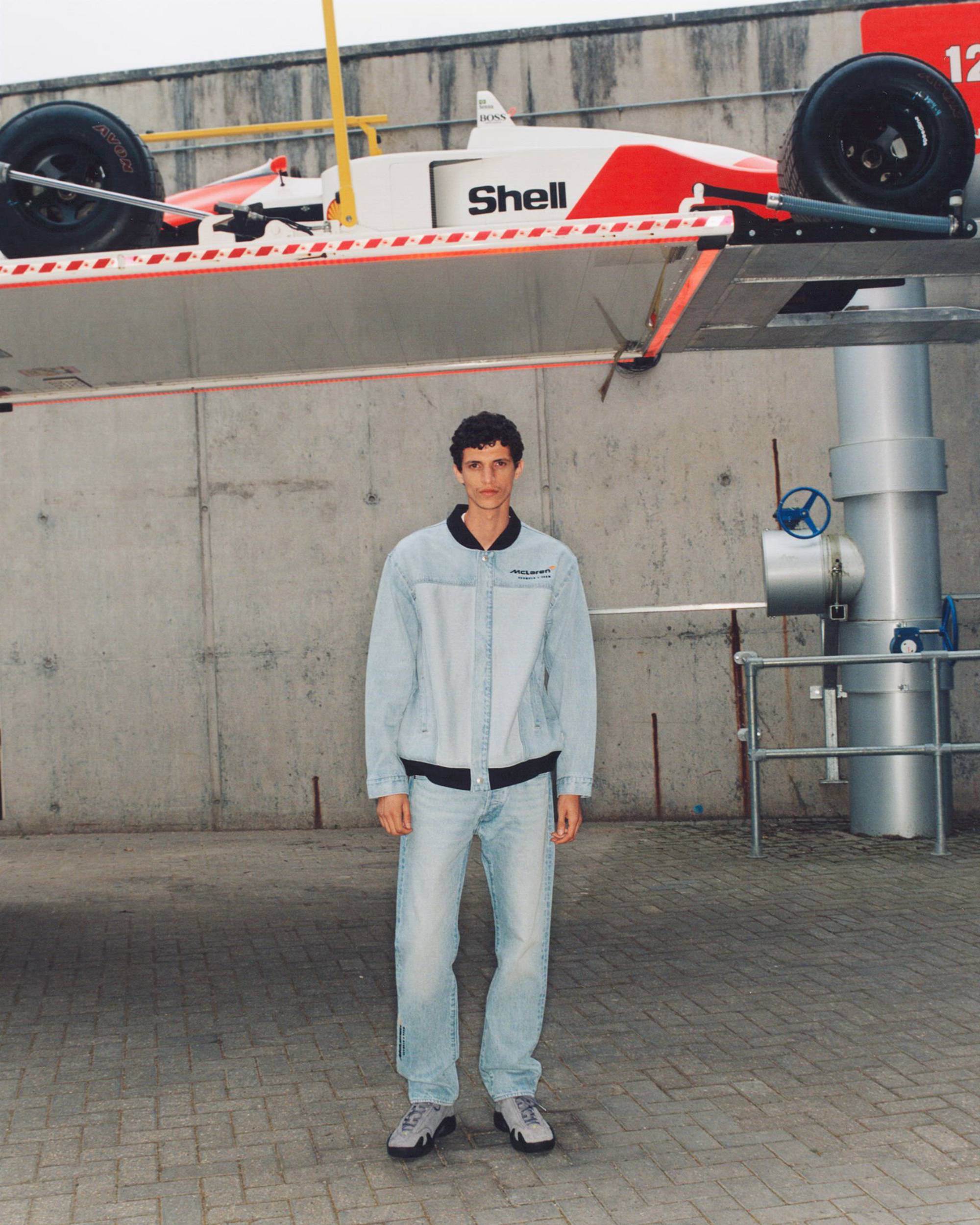 Rotating images of models wearing pieces from the Levi's® x McLaren Racing collection against a concrete bkgd featuring McLaren race car