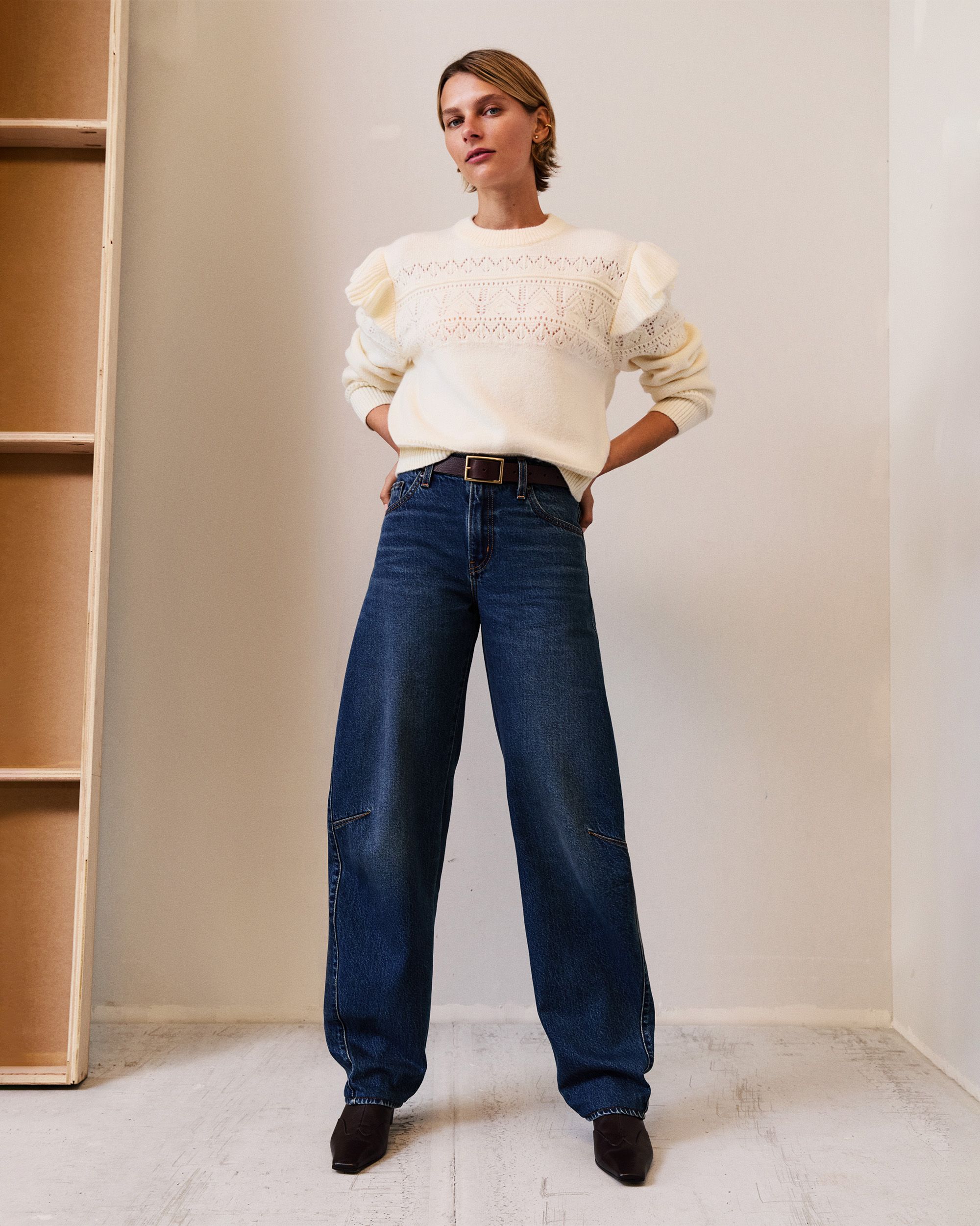 Model with short hair wearing dark wash denim and white pointelle sweater