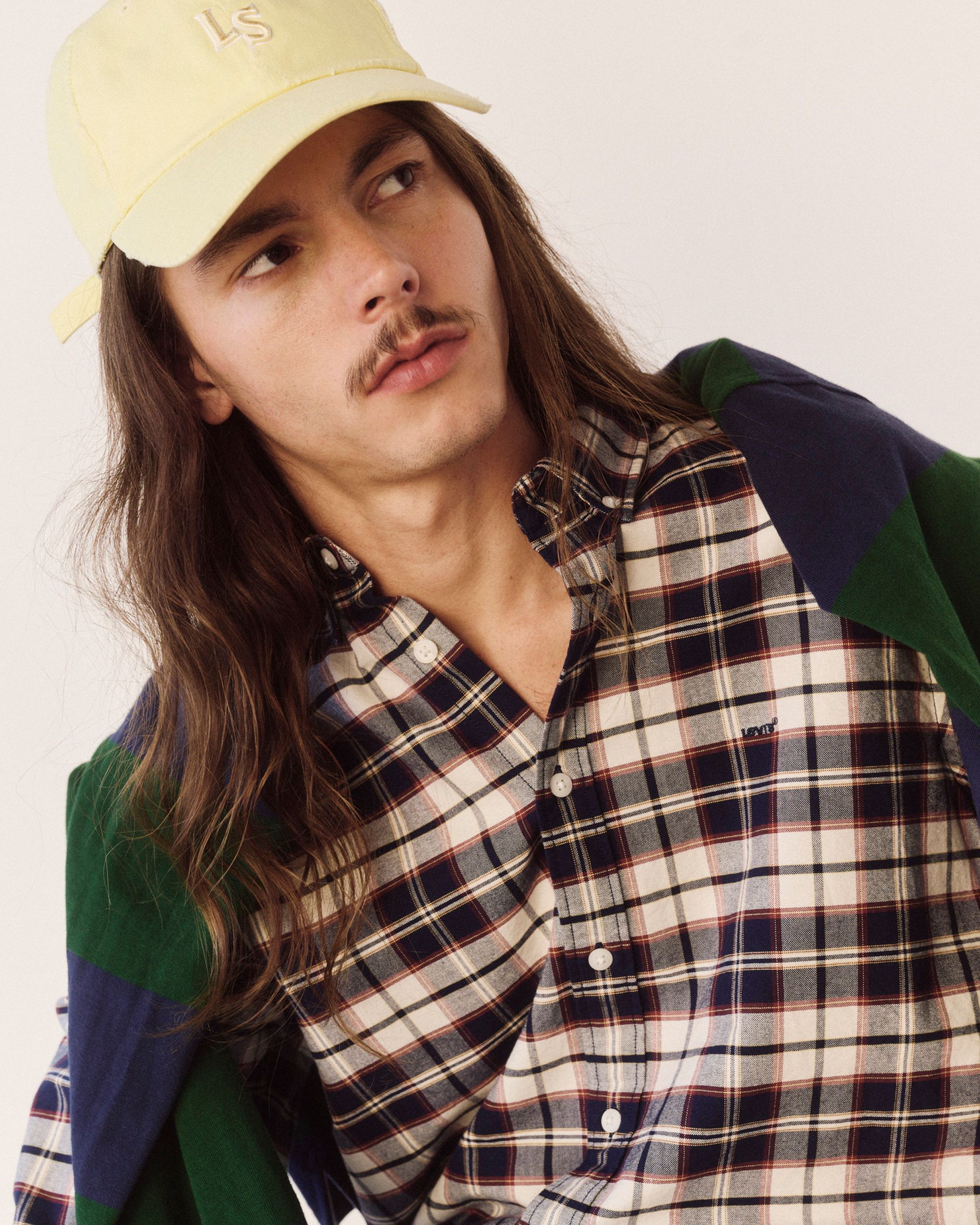 Model in plaid button up, striped polo & yellow hat