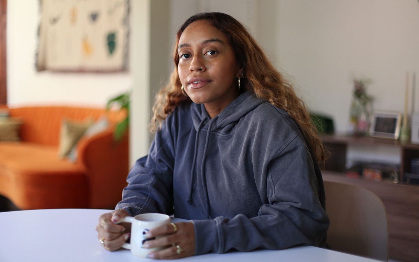 Portrait of Evelynn Escobar-Thomas sitting at her kitchen table with a white mug in her hands.