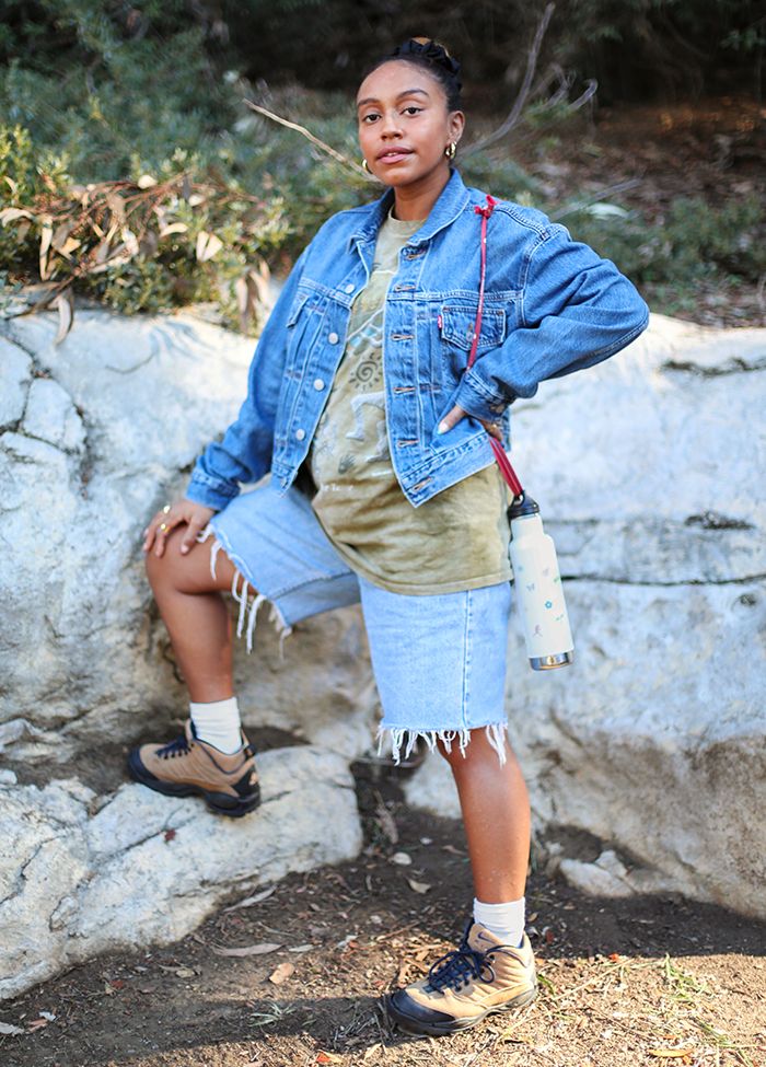 Photo of Evelynn Escobar-Thomas outdoors, wearing a Levi's Trucker Jacket, a tie-dye shirt, and denim cut-offs with hiking shoes.