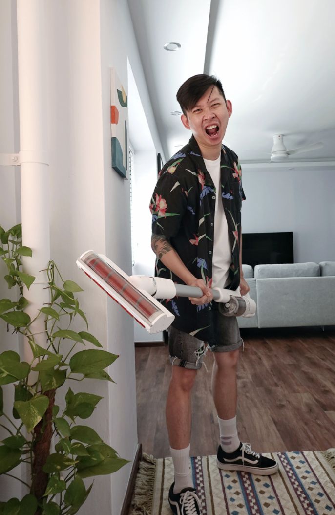 Photo of Mark Chan brandishing a portable vacuum. He is wearing a tropical-print Cubano shirt over a white tee with cut-off denim shorts and white socks with black Vans.