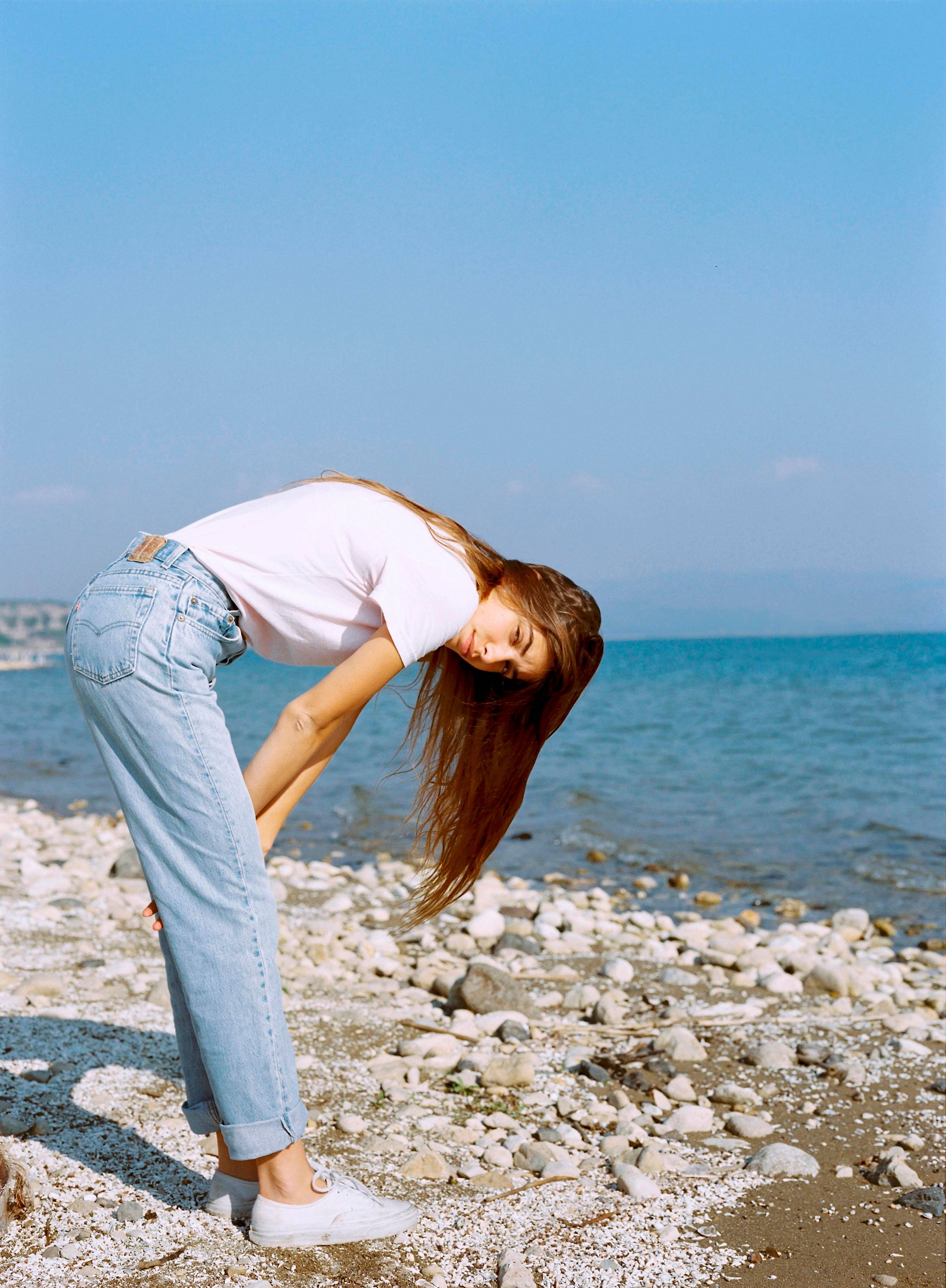 woman standing bent over and the ocean in the background.